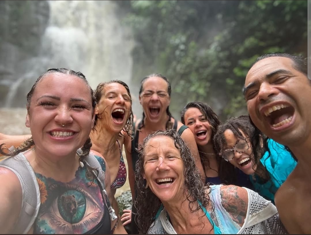 Group of joyful retreat guests soaked at the base of a jungle waterfall