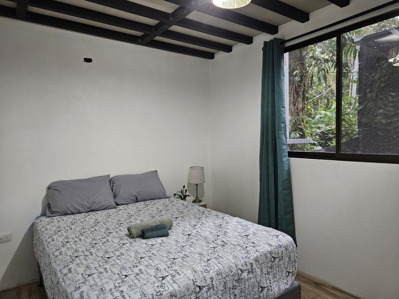 Bedroom with wooden ceiling beams and jungle-facing window