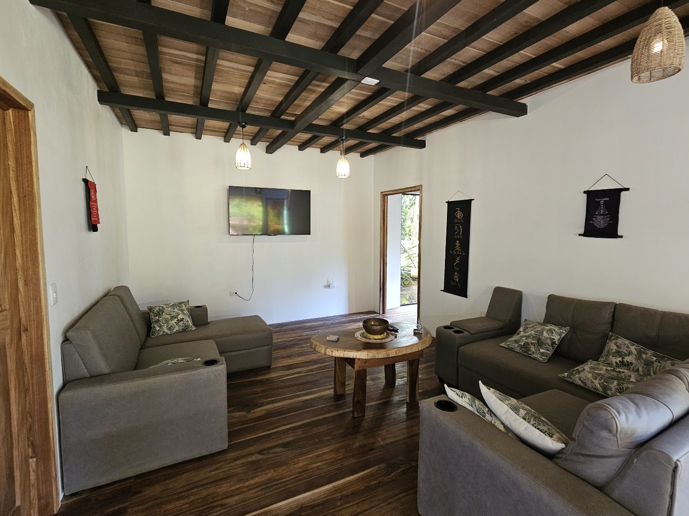 Bright living room with sofas, wooden beams, and jungle windows